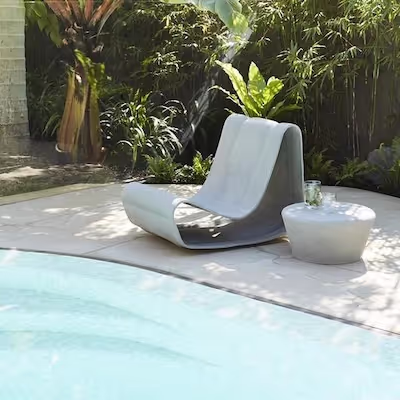 Swisspearl Guhl‑Stuhl und Porto Beistelltisch mit Glas auf sonniger Poolterrasse, umgeben von Bambus und Palmen.