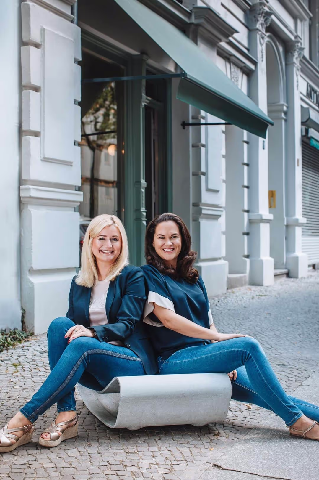 Karolin Frieser und Julia Müller sitzen auf einem Guhl Stuhl auf dem Bürgersteig.